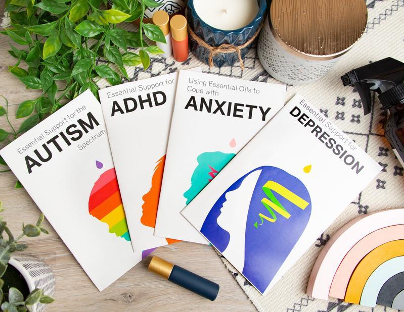 The Essential Support booklets highlighting autism, ADHD, anxiety and depression fanned out and pictured with some essential oil roller bottles, plants and candles.