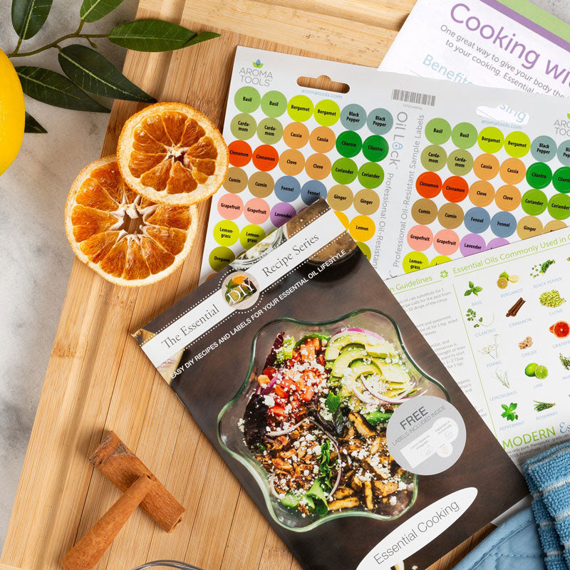 The Essential Cooking booklet, Oil Lock cooking collection sticker labels, and other cooking with essential oil handouts on a cutting board.