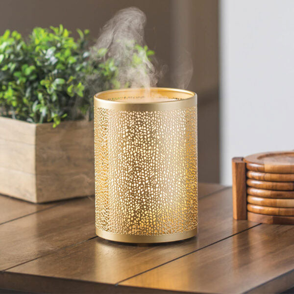 Gold essential oil diffuser sitting on a coffee table with wooden coasters and small plant.