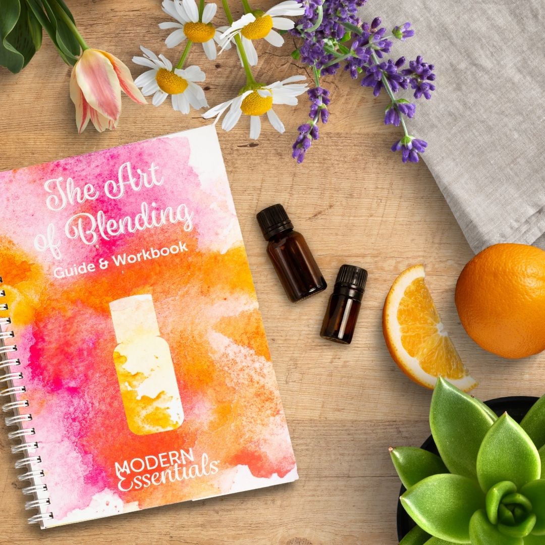 The Art of Blending Guide and Workbook with essential oil vials, oranges, and some flowers.