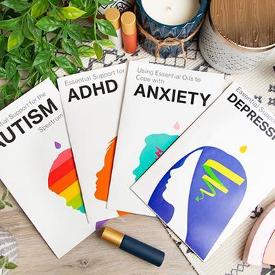 The Essential Support booklets highlighting autism, ADHD, anxiety and depression fanned out and pictured with some essential oil roller bottles, plants and candles.