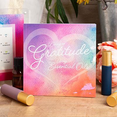 The "Living with Gratitude Using Essential Oils" booklet with matte roller bottles and some plants.