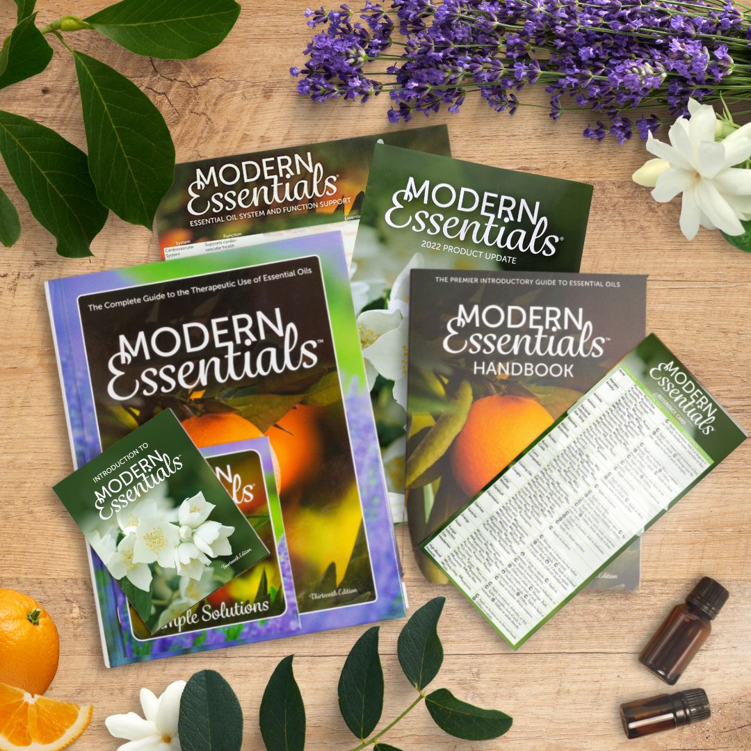 The Modern Essentials Family (14th edition) laid out on the wood table with essential oil vials, plants, and oranges along the borders.