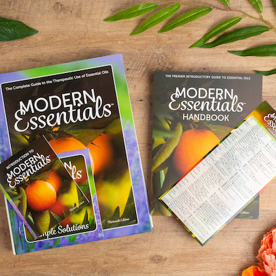 The Modern Essentials Family (13th Editions) sitting on a wood table with some plants.