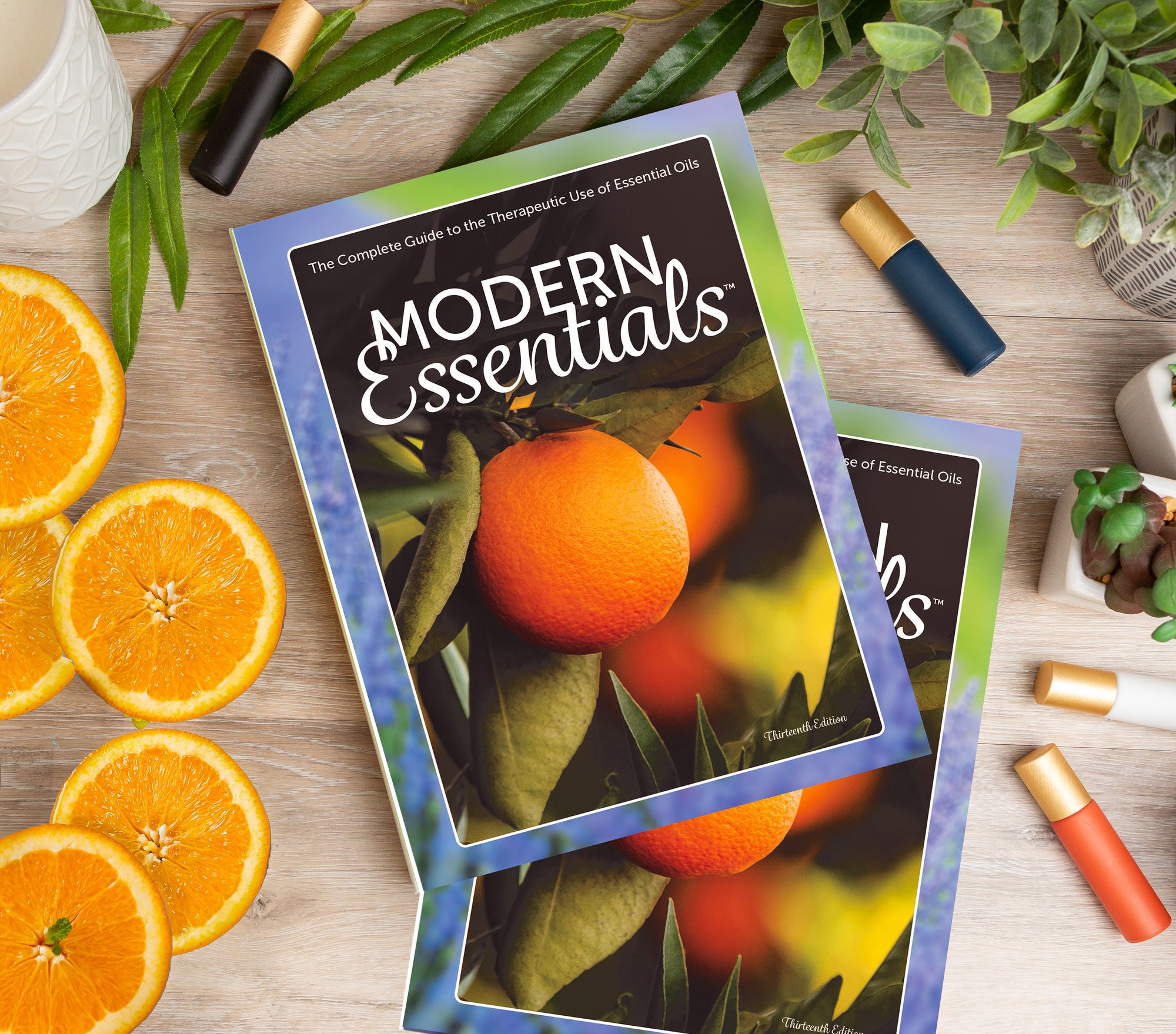 The hardcover Modern Essentials (13th Edition) on a table with roller bottles and orange slices.